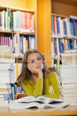 Tired beautiful student studying between piles of books