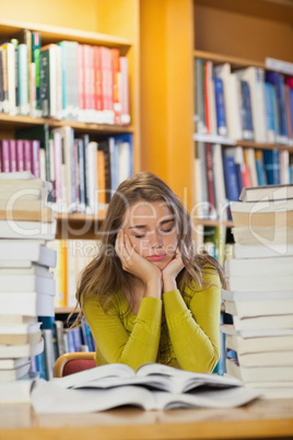 Tired beautiful student studying between piles of books with clo