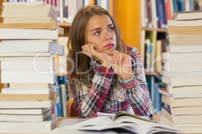 Serious pretty student sitting between piles of books