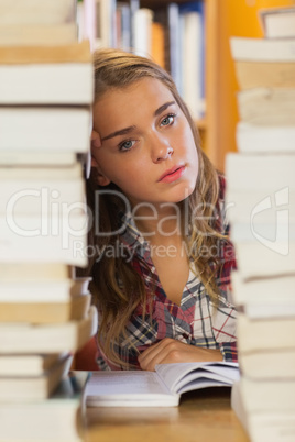 Unsmiling pretty student studying between piles of books