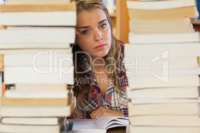 Stern pretty student studying between piles of books