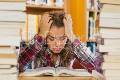 Irritated pretty student studying between piles of books