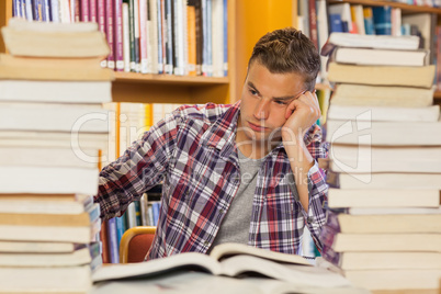 Frustrated handsome student studying between piles of books