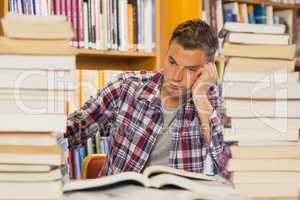 Frustrated handsome student studying between piles of books