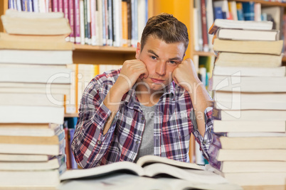 Irritated handsome student studying between piles of books