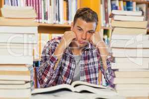 Irritated handsome student studying between piles of books