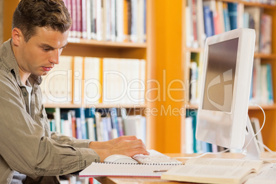 Handsome serious student using computer reading notes