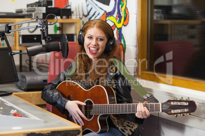 Smiling beautiful singer recording and playing guitar