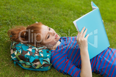 Gorgeous focused student lying on grass reading notes
