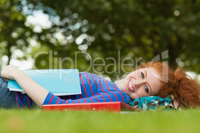 Gorgeous smiling student lying on grass reading notes