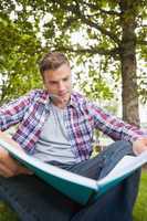 Handsome serious student sitting on grass studying