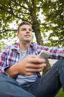 Handsome happy student sitting on grass texting