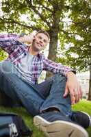 Handsome happy student sitting on grass phoning