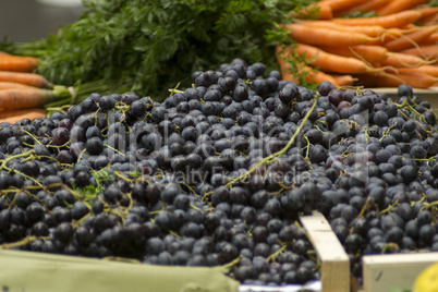 Rote Weintrauben vor orangenen Möhren auf dem Wochenmarkt