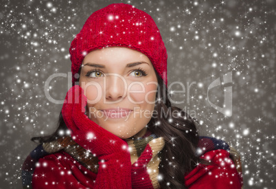 mixed race woman wearing winter hat and gloves enjoys snowfall.
