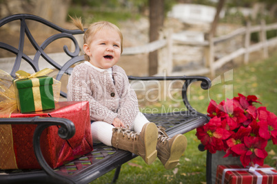 young toddler child sitting on bench with christmas gifts outsid