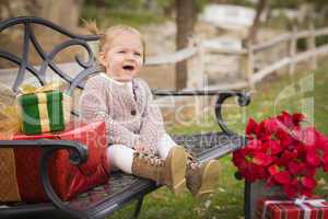 young toddler child sitting on bench with christmas gifts outsid
