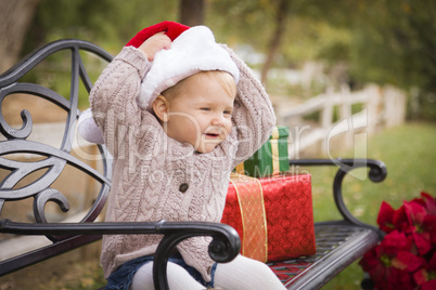 young child wearing santa hat sitting with christmas gifts outsi