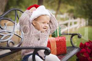 young child wearing santa hat sitting with christmas gifts outsi
