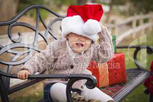 young child wearing santa hat sitting with christmas gifts outsi