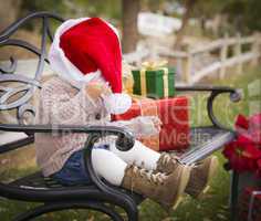 young child wearing santa hat sitting with christmas gifts outsi