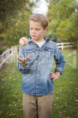 handsome young boy tossing up baseball in the park