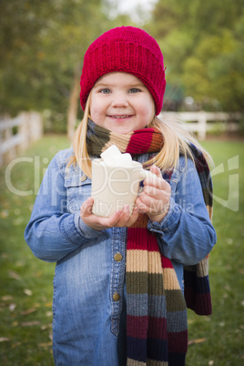 cute young girl holding cocoa mug with marsh mallows outside