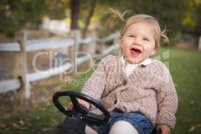 young toddler laughing and playing on toy tractor outside