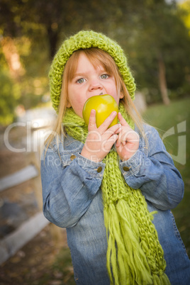 young girl wearing green scarf and hat eating apple outside