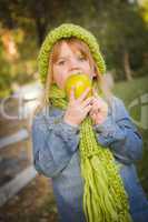 young girl wearing green scarf and hat eating apple outside