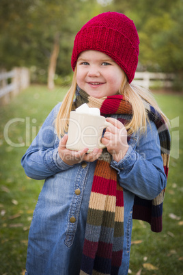 cute young girl holding cocoa mug with marsh mallows outside