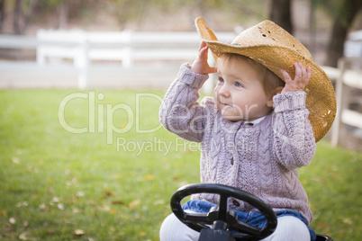 toddler wearing cowboy hat and playing on toy tractor outside