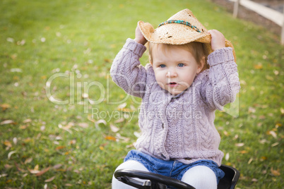 toddler wearing cowboy hat and playing on toy tractor outside