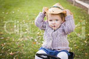 toddler wearing cowboy hat and playing on toy tractor outside