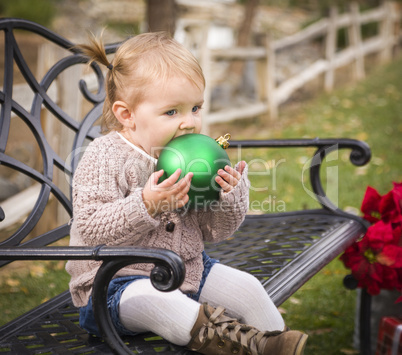 toddler child sitting on bench with christmas ornament outside