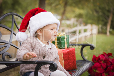 young child wearing santa hat sitting with christmas gifts outsi