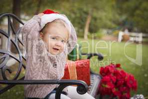 young child wearing santa hat sitting with christmas gifts outsi