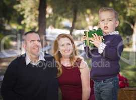 young boy holding christmas gift in park while parents look