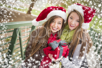 two smiling women santa hats holding a wrapped gift