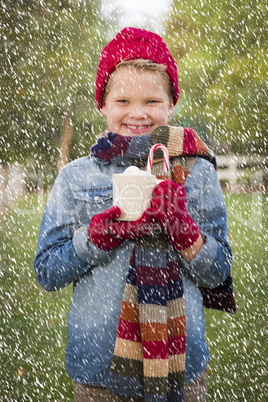 young boy in warm clothing holding hot cocoa mug outside