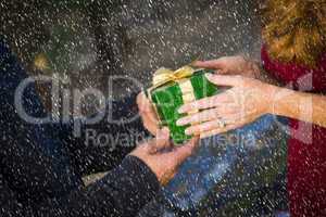 hands of man and woman exchanging christmas gift in snow