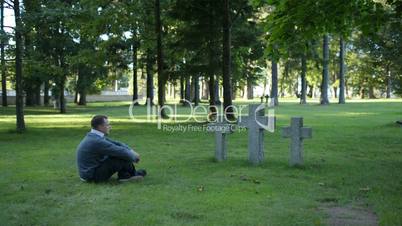 Man sitting mourning in front of three crosses