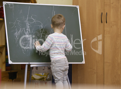 little boy drawing on a chalkboard at kindergarten