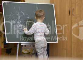little boy drawing on a chalkboard at kindergarten