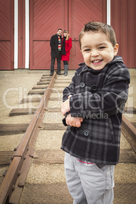 mixed race boy at train depot with parents smiling behind