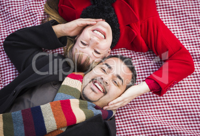 mixed race couple wearing winter clothing on blanket in park