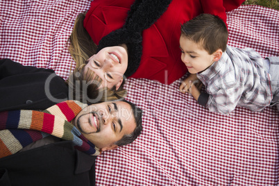 family in winter clothing laying on their backs in park
