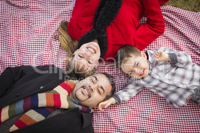 family in winter clothing laying on their backs in park