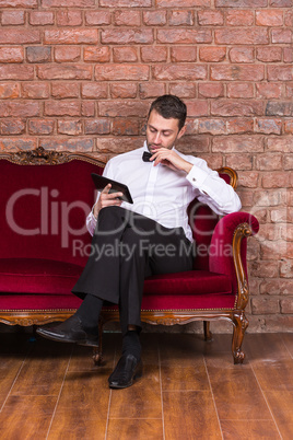 businessman lying on a settee and reading tablet