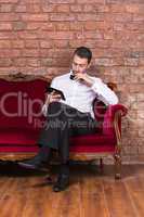 businessman lying on a settee and reading tablet